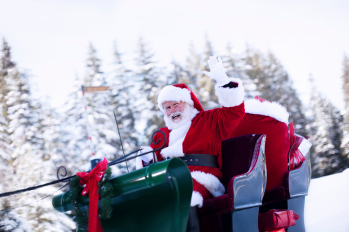 Santa Claus waving as he drives his sleigh through the snow. Sack of presents in the back. Copy space. CLICK FOR SIMILAR IMAGES AND LIGHTBOX WITH SEASONAL IMAGES.