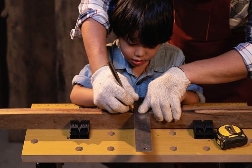 Carpenter teaching son to practice learning and Concentrated to work with wood in his workshop, Success is a learnable skill, Practice learning for kids concept. Selective focus on hand.