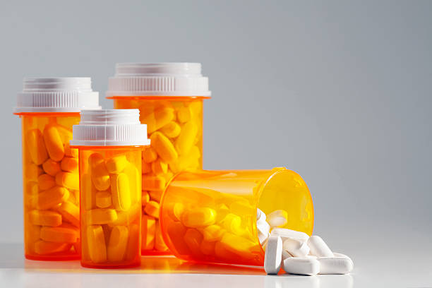 Four full prescription bottles with one spilling medication Prescription medication spilling from an open bottle. This macro shot shows caplets or pills in the opening of a medicine bottle with other standing bottles in the background. The photo includes open space for your copy. medium group of objects stock pictures, royalty-free photos & images