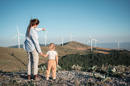 Back to nature. Family with Gen Alpha kid hiking among wind turbines in the mountains. Renewable energy in everyday life.