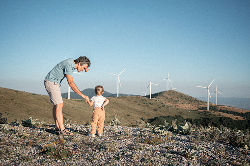 Back to nature. Family with Gen Alpha kid hiking among wind turbines in the mountains. Renewable energy in everyday life.