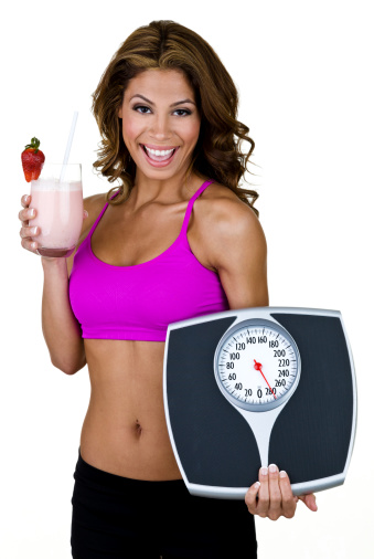 Vertical composition of a pretty woman wearing fitness clothing and holding a scale and fruit smoothie for a weight loss concept 