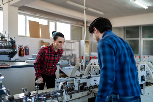 Male and female engineers checking and adjusting machines in production workshop.