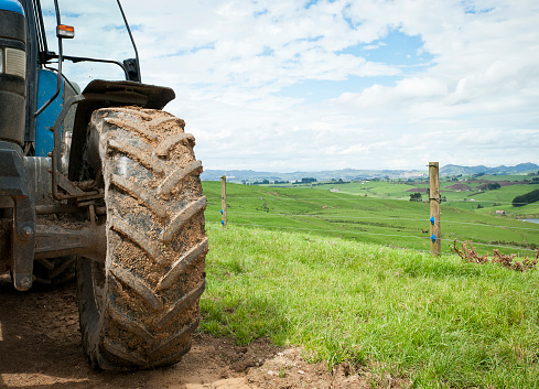 A muddy front tyre of a tractor against a rolling rural background.  Focus on the foreground.  Ample sky space left for copy.