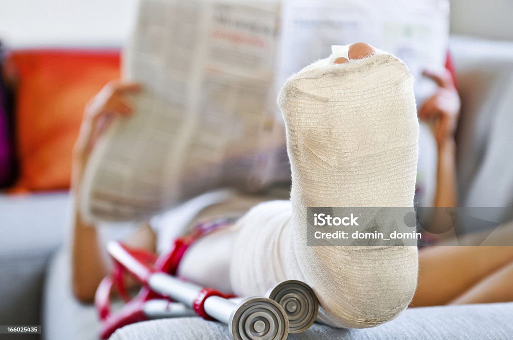 Mulher com Perna Quebrada deitado no sofá e jornal de leitura - Foto de stock de Gesso royalty-free