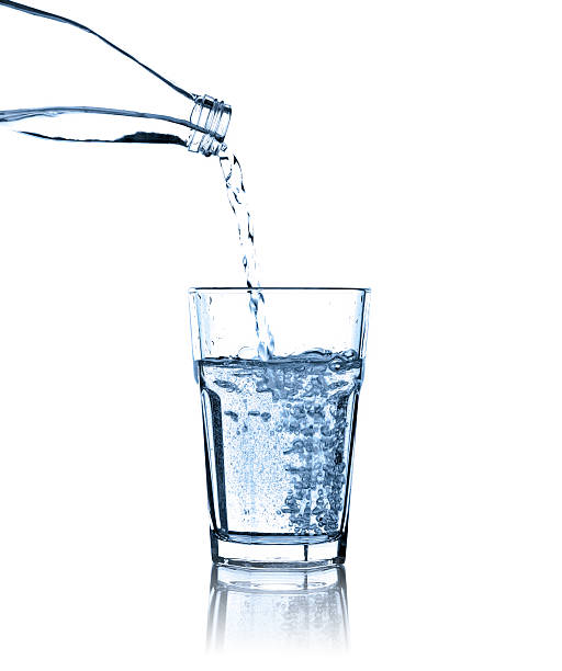 agua vertiendo de botella en vidrio, foto de estudio aisladas - agua purificada fotografías e imágenes de stock