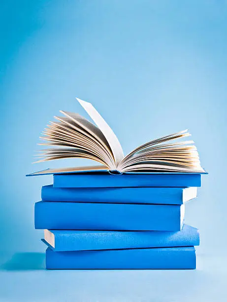 Photo of Opened book on top of stack of blue books, knowledge