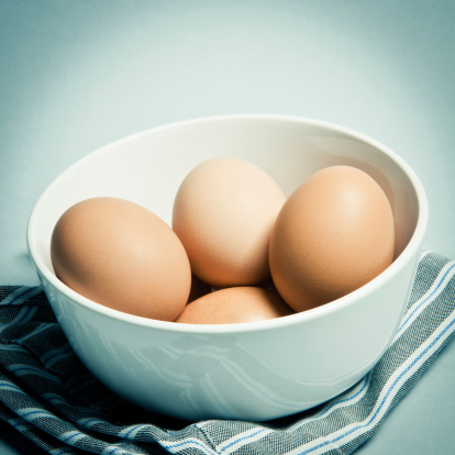Group of fresh or boiled eggs in a white bowl standing on cloth, square. Studio shot