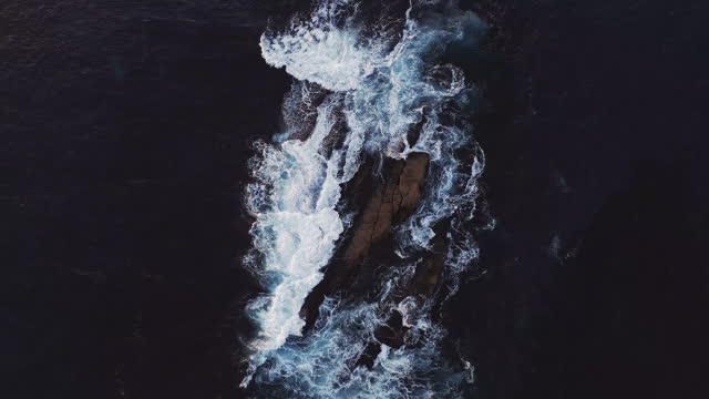 Crane shot above raw ocean waves surging over rocks