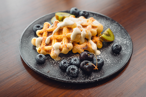 Waffles in a plate with blueberries, kiwi, bananas, cherries and cream.