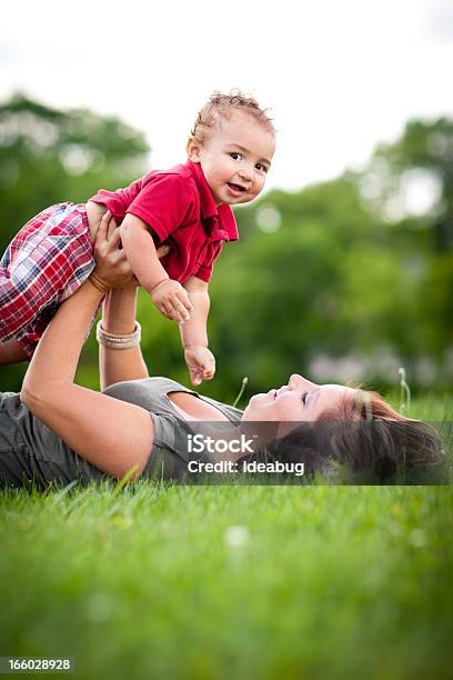 Glückliche Mutter Holding Sohn Beim Liegen Im Gras Im Stockfoto und mehr Bilder von 12-17 Monate