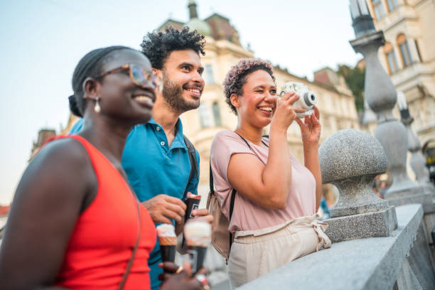 Exploring the city, friends savor ice cream and snap photos with analog cameras on a picturesque bridge, creating lasting memories.