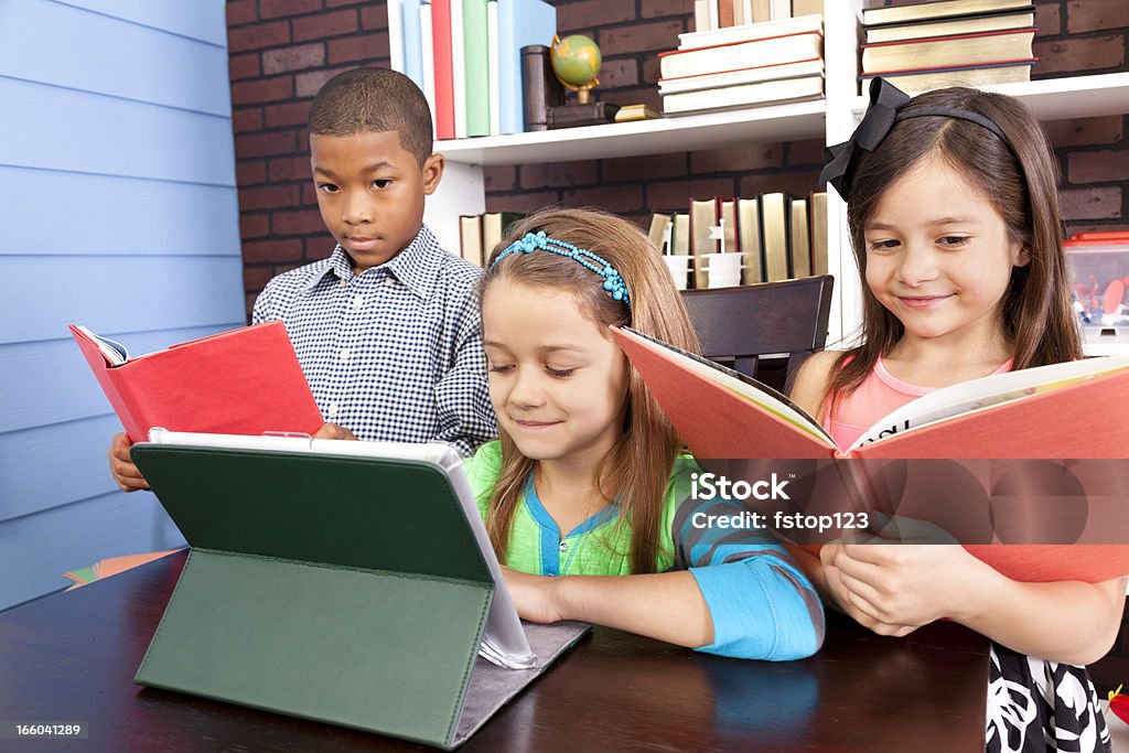 Multi-ethnique élèves de primaire. École en configuration salle de classe. Tablette numérique et des livres. - Photo de Livre libre de droits