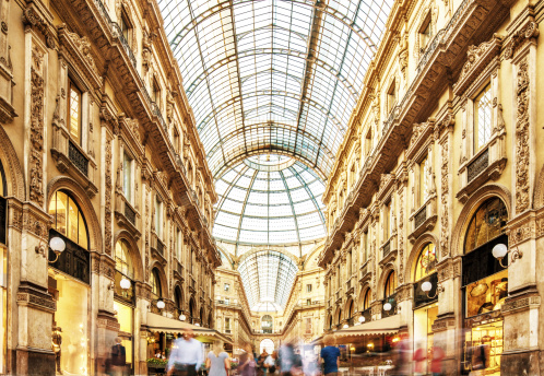 Galleria Vittorio Emanuele II in Milano, Italy, the famous luxury shopping mall, showing the spectacular view of an almost golden gate to luxury. Long exposure with motion blurred people walking along the shops and restaurants. Milan, Lombardy, Italy