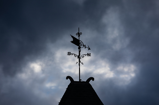 silhouette of an antique weather vave atop an old city hall in rural Michigan as an evening storm moves in.