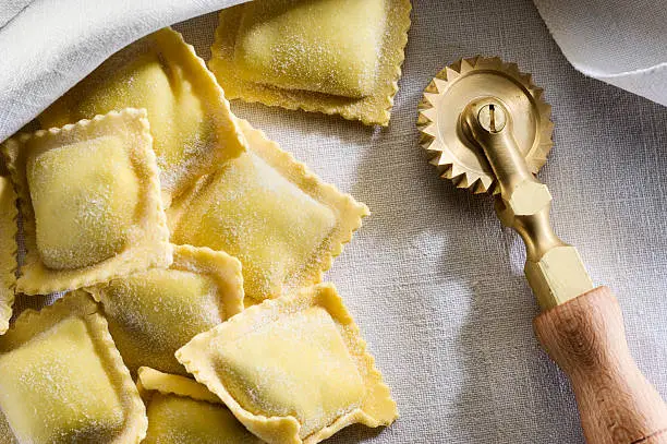 Some fresh ravioli on a linen cloth with a brass cutter for pasta.