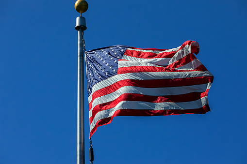 detailed photo of a US flag flying in the wind against a perfect blue sky