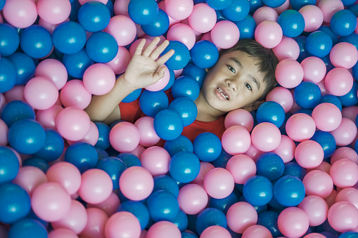 A boy pops his head out of a pink and blue ball.