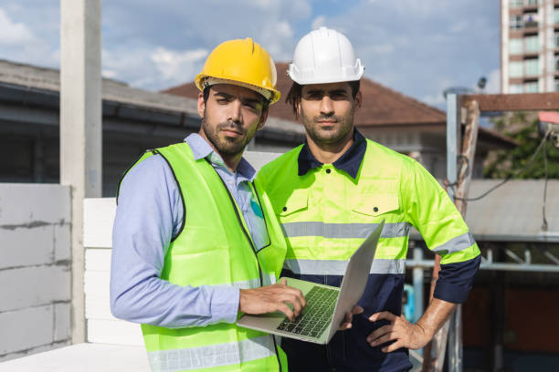 istock Professional construction engineer team, Two man engineer wear uniform holding laptop looking at camera standing at construction site. 1660508003