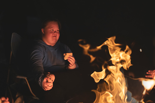 A teenage girl with Down syndrome enjoying a campfire while camping with her family