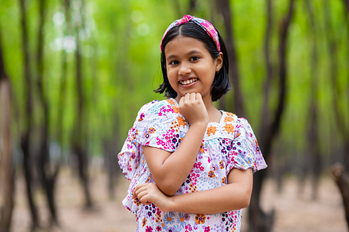 A pretty cute Indian girl child smiling and looking at camera in green nature background
