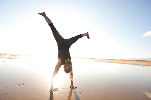 Full length of a woman does a handstand on the beach during a summer day