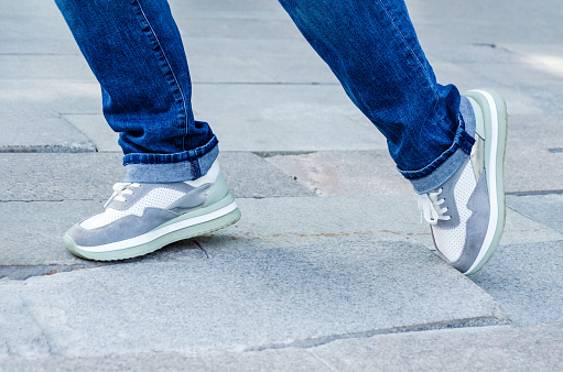 close-up of a woman's feet in jeans and sneakers tripping over unevenly laid paving slabs. Accident, injury on a walk due to poor road surface.