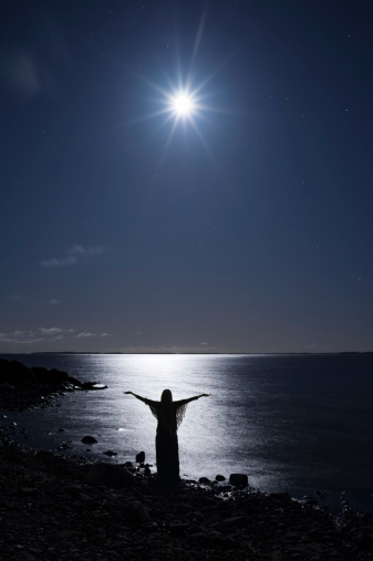 Woman standing on rocky shore and greeting the moon.