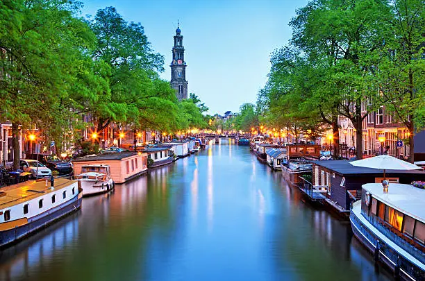 a canal with house boats in the city of Amsterdam at dusk