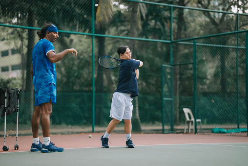 Asian Chinese Down syndrome man learning from male coach trainer playing tennis during weekend morning
