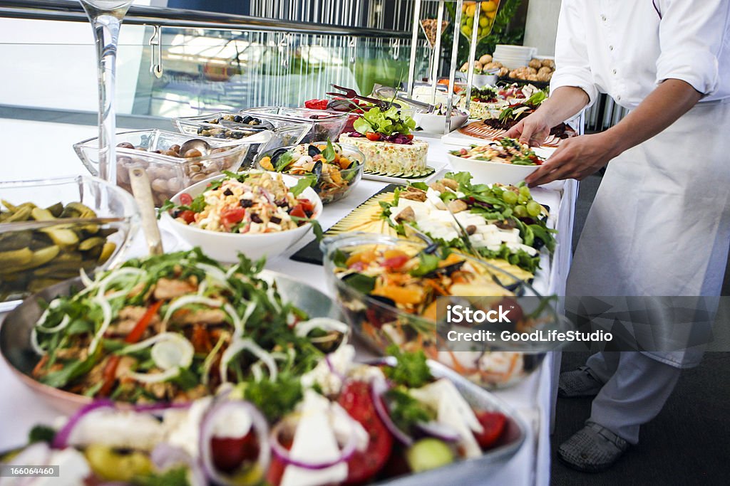 Waiter serving a buffet table Waiter serving a large buffet table full of delicious food. Unrecognizable Caucasian male, professional in white apron and uniform. Food And Drink Industry Stock Photo