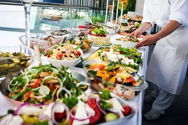 Waiter serving a large buffet table full of delicious food. Unrecognizable Caucasian male, professional in white apron and uniform.