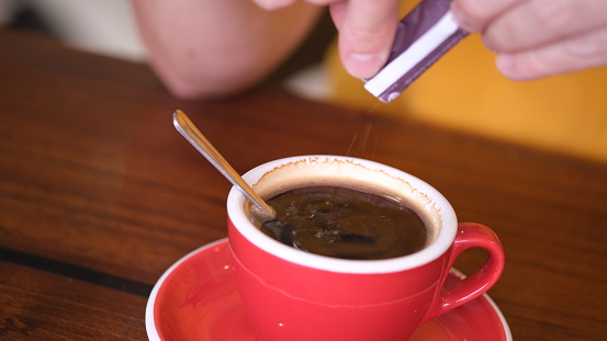 Hand is pouring sugar sachet into a cup of coffee.