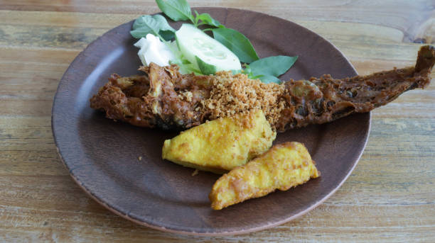 istock Savor Pecel Lele or pecak lele East Java's delight. Deep fried catfish with sambal, paired with crisp cucumbers, cabbage, lettuce, basil leaf, fried tofu and tempeh. A flavorful Indonesian indulgence. 1660708281