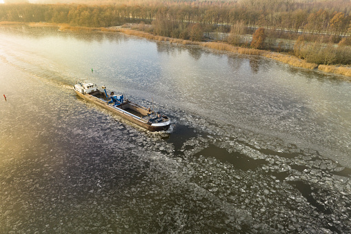 Freight ship barge ploughing through ice on a frozen Drontermeer lake during a cold winter day in The Netherlands