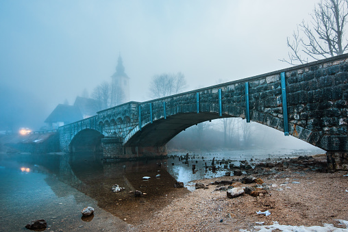 Old stone bridge at Bohinj lake in foggy morning, tranquil scene from Slovenia's travel destination in dawn, selective focus