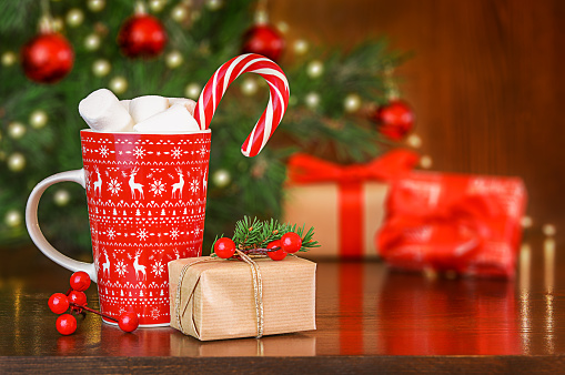 Christmas presents and cup of hot chocolate with marshmallows and red candy cane on wooden festive background