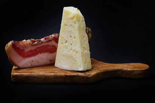 bacon and pecorino romano on a wooden chopping board with a black background