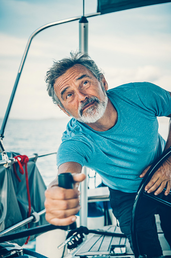 Skipper sailing on sailboat trimming the jib sail with rotating the handle. Taken by Sony a7R II, 42 Mpix.