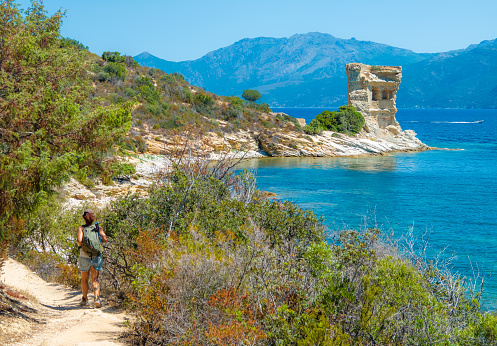 Corse, France - 2 July 2023 - Corsica is a big touristic french island in Mediterranean Sea, with beautiful beachs and mountains. Here a view of the Sentier du littoral from Saint-Florent at Plage de Lotu with girl tourist and old tower