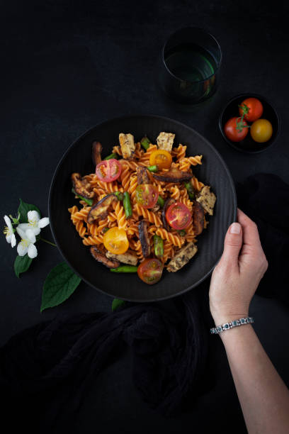 istock Fusilli pasta with mushrooms, asparagus and cherry tomatoes as closeup on a modern design plate and dark background 1660866923