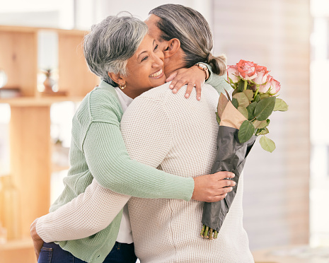 Mature couple, flowers and hug at home for anniversary, birthday or valentines celebration. Surprise, love and roses or bouquet with a man and woman for healthy marriage, happiness and romance