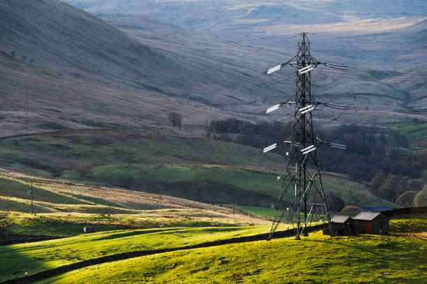 Large electricity pylon in a shaft of sunlight in the English Lake District. Late afternoon light with a hazy view of a shaded valley in the background.