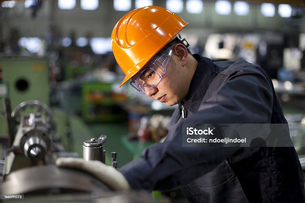 Technician in uniform and hard hat working on a machinery Technician working in factory Machinery Stock Photo