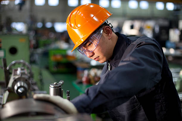 Technician in uniform and hard hat working on a machinery Technician working in factory lathe stock pictures, royalty-free photos & images