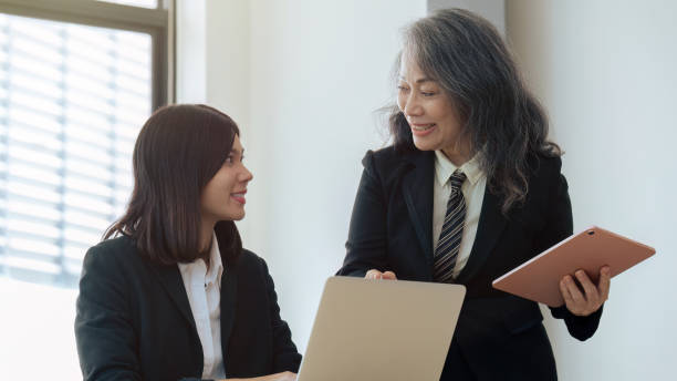 istock young financial assistant working on laptop while senior professional standing and giving investment advise 1660914109