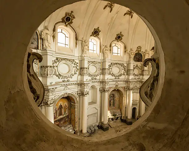 Ornate interior of Baroque Church of Santa Chiara with ribbed stucco ceiling and walls, in white with gold bas-relief,, seen through roundel windows of upper choir balcony, Noto, Sicily, Italy