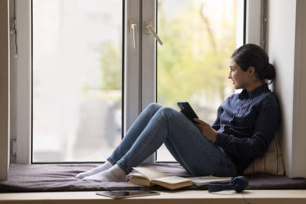 istock Indian woman hold smartphone staring out window resting on windowsill 1660919064