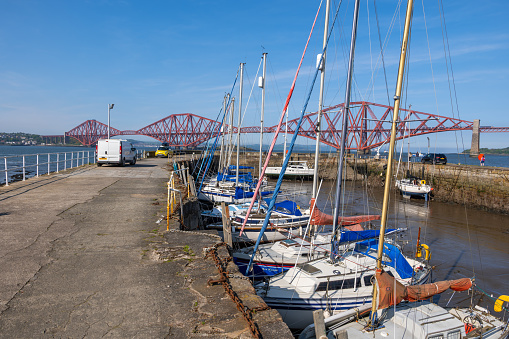 South Queensferry, Scotland, UK - May 13, 2023 - Pier and harbor with sailing boats at the Forth Bridge over Firth of Forth estuary.