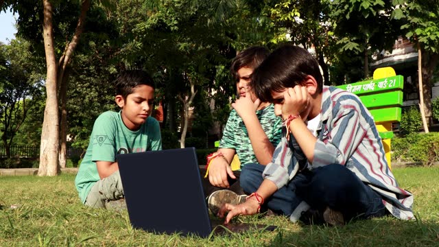 Children using laptop outdoor in the park and playing with rubics cube